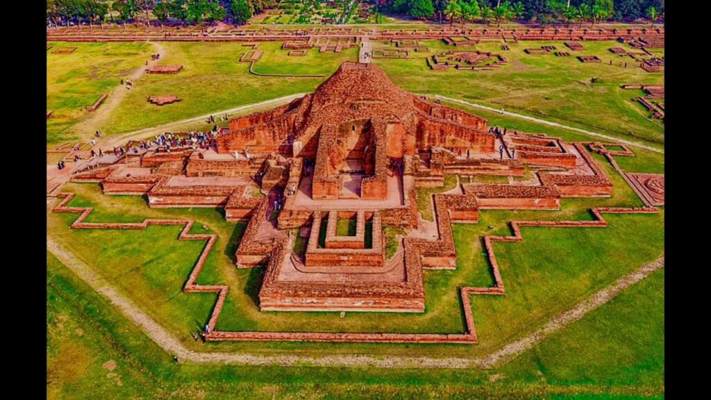 The wide grassy courtyard of Somapura Mahavihara with the perimeter wall of monastic cells in the background.